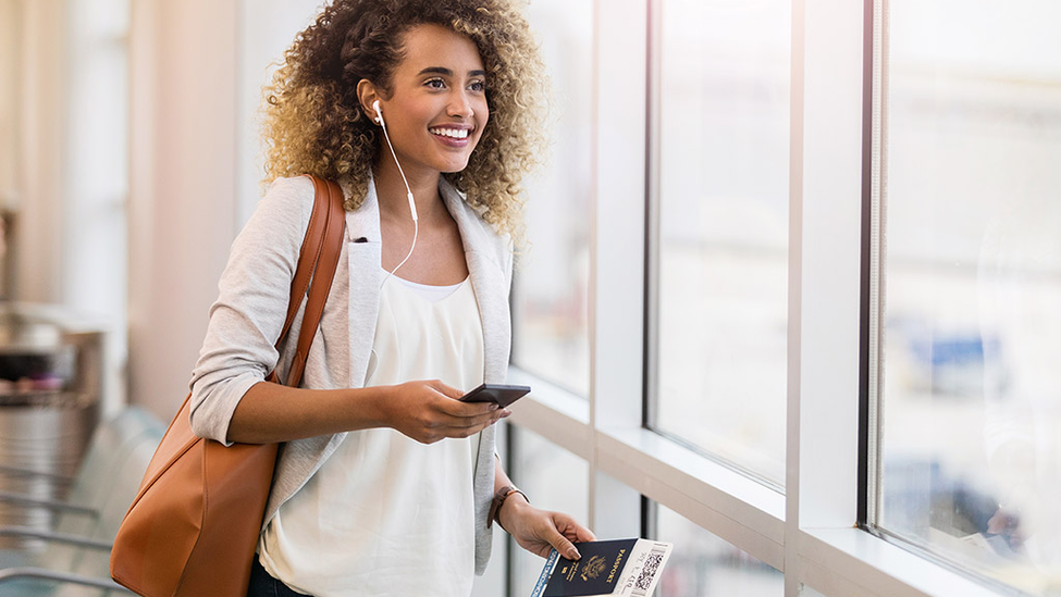 Young woman smiling walking through and airport, carrying a passport.