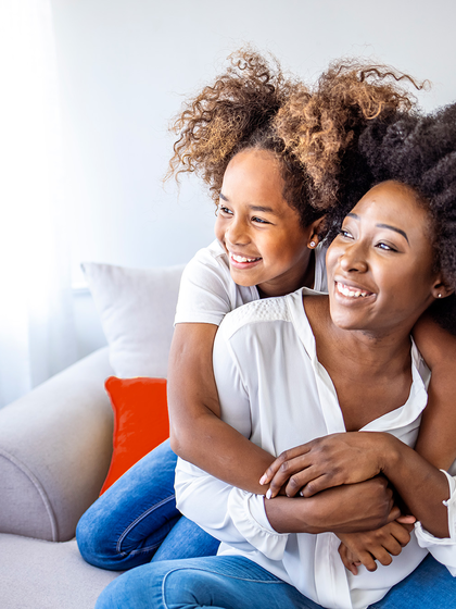 Daughter hugging mother from behind while sitting on a couch. 