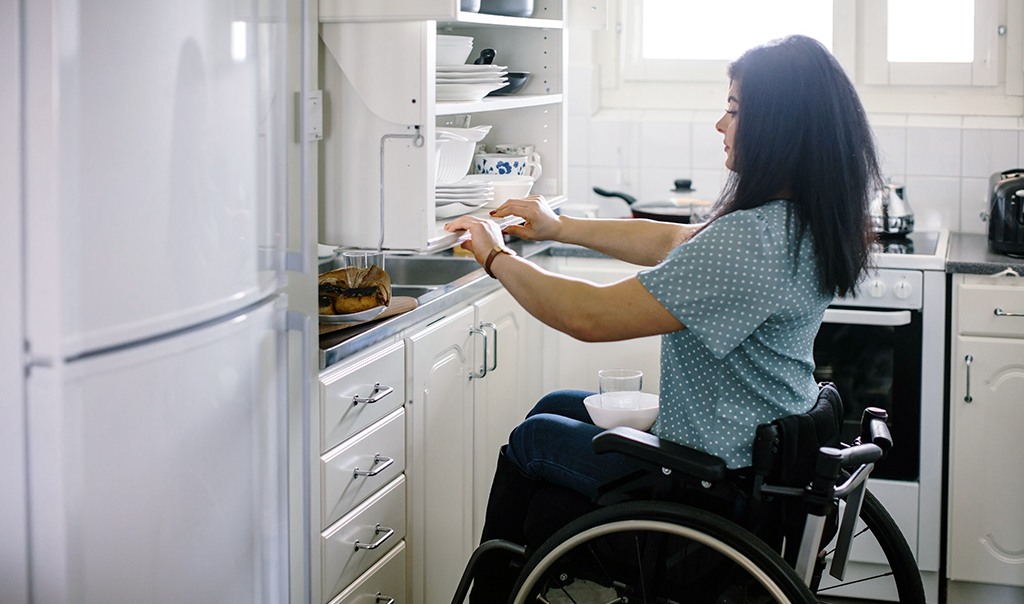 Woman in wheelchair pulling modified cabinet in her kitchen
