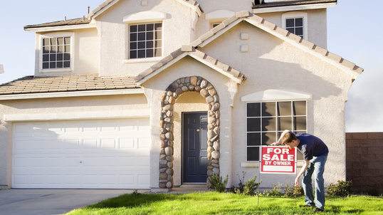 Person putting for sale by owner sign in front of house.