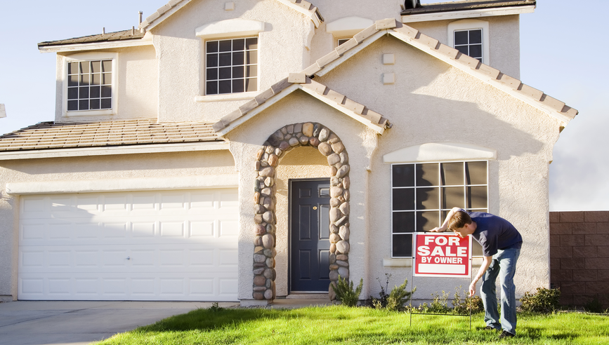 Man placing home for sale by owner sign in yard.