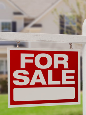 A "For Sale" sign hangs in front of a suburban house.