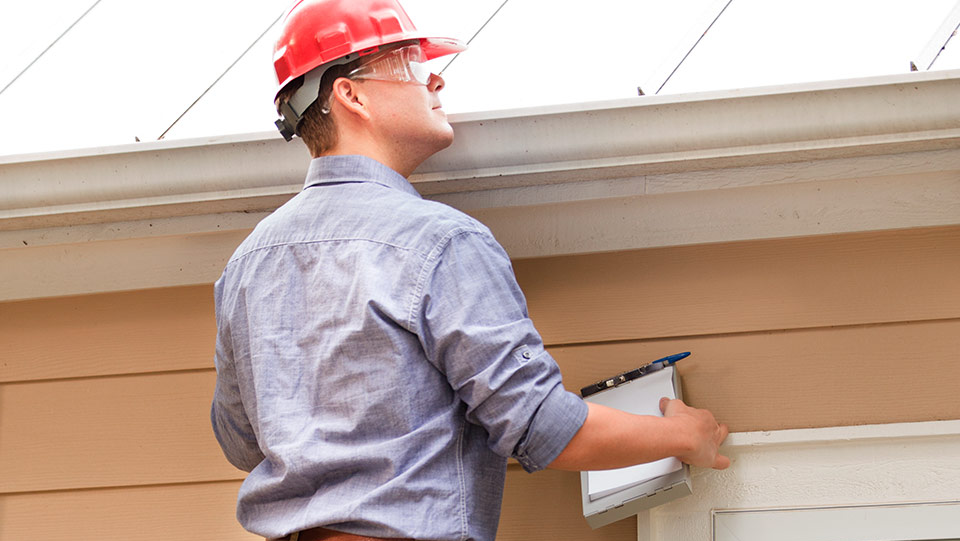 Home inspector on a ladder inspecting the roof of a home.