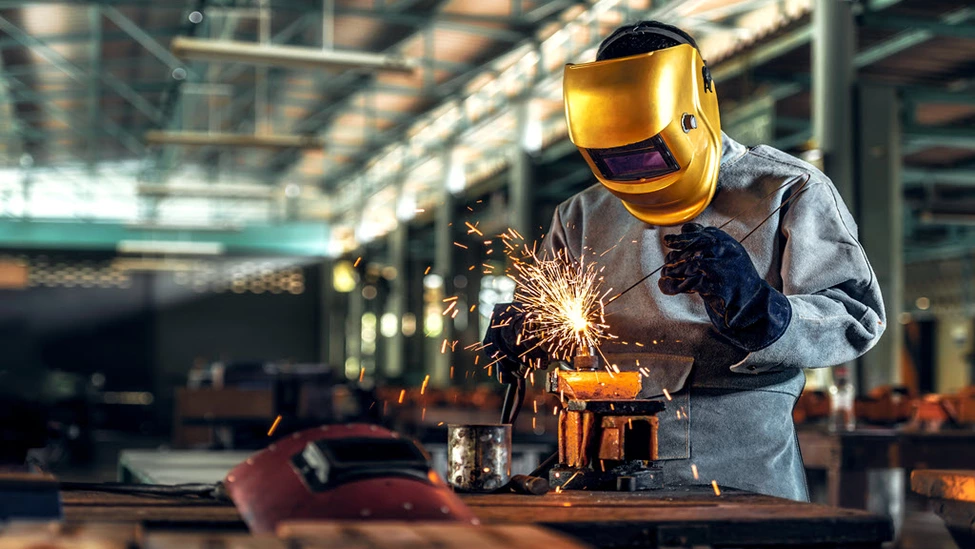 Man in gold mask welding in a factory.