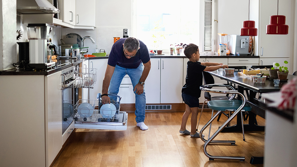 Father and son loading dishwasher in their kitchen.