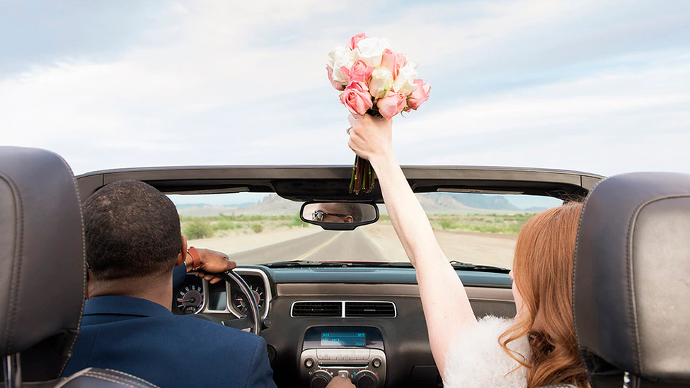 Husband and wife driving off in a convertible car after getting married.