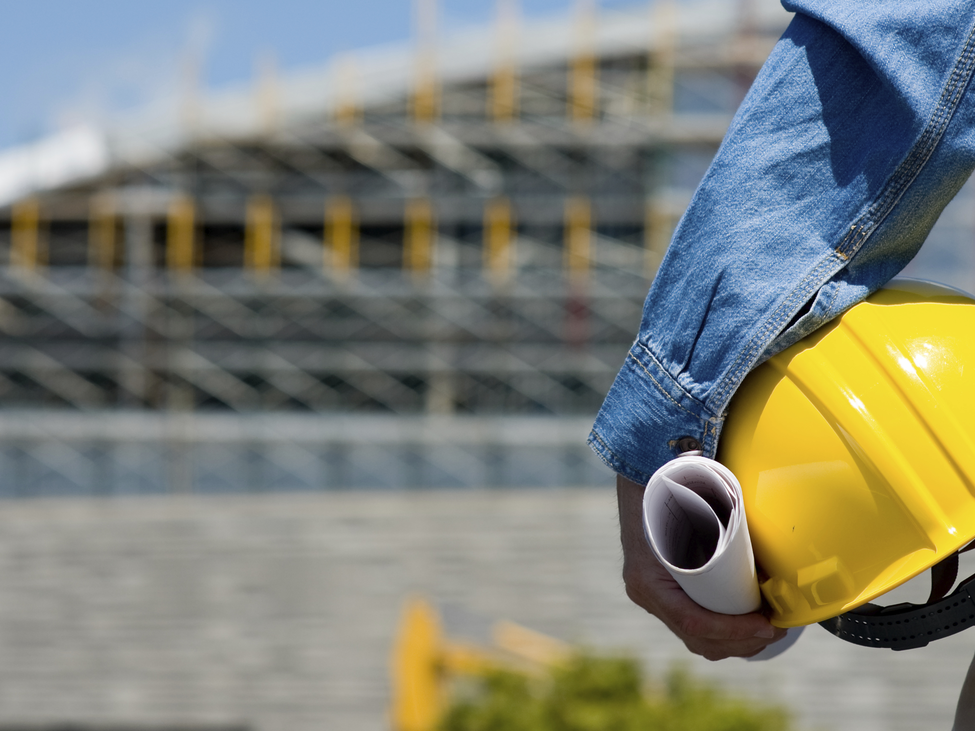 Construction worker with hard hat and design standing in front of a construction site