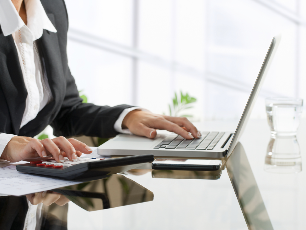 A legal professional does calculations with a laptop and desktop calculator.