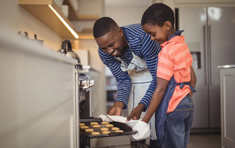 Image of man and son taking cookies out of the oven in their home.