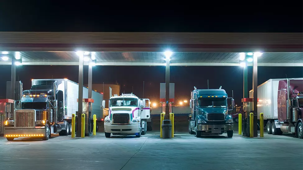 Trucks at a truck stop lined up at a gas station.