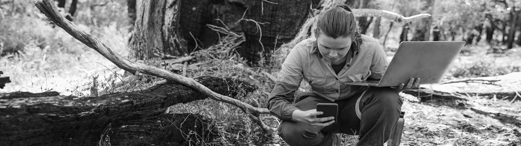 A woman with a phone and laptop inspecting a wildfire.
