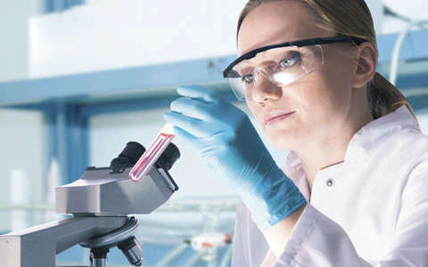 A lady in laboratory safety wear looking at an unknown substance.