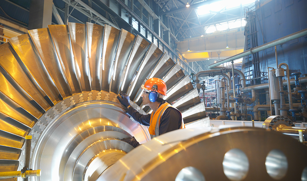 A man in safety gears fixing a big machine with gears.