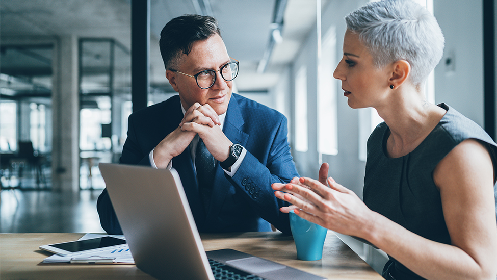 Two business people sitting in front of a laptop discussing risk management.