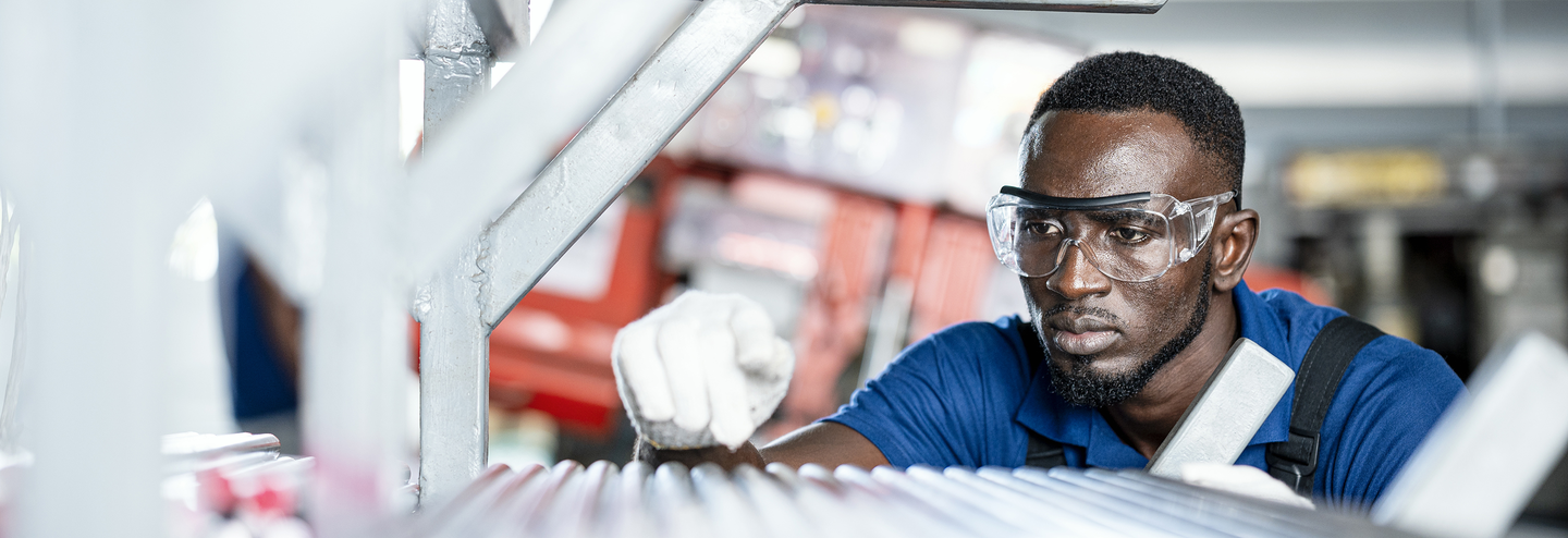 A quality control engineer inspects steel pipe material for production on shelf rack at factory warehouse.