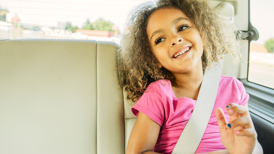 Smiling child sitting safely in the back seat of a car.