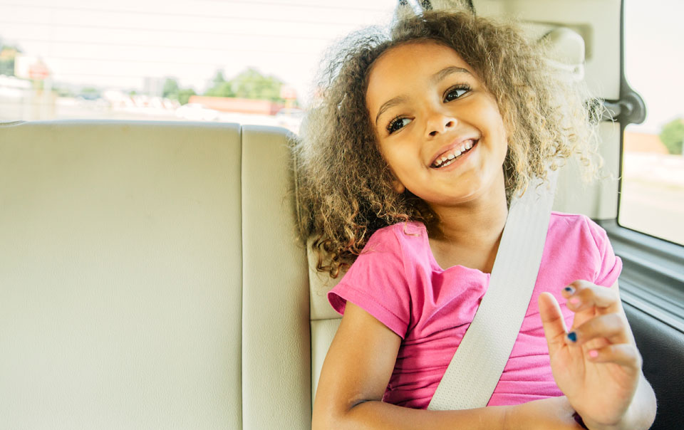 Smiling child sitting safely in the back seat of a car.