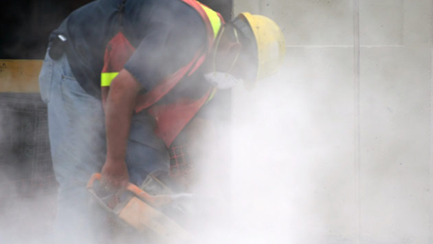 Working using saw that is raising dust in construction work site.