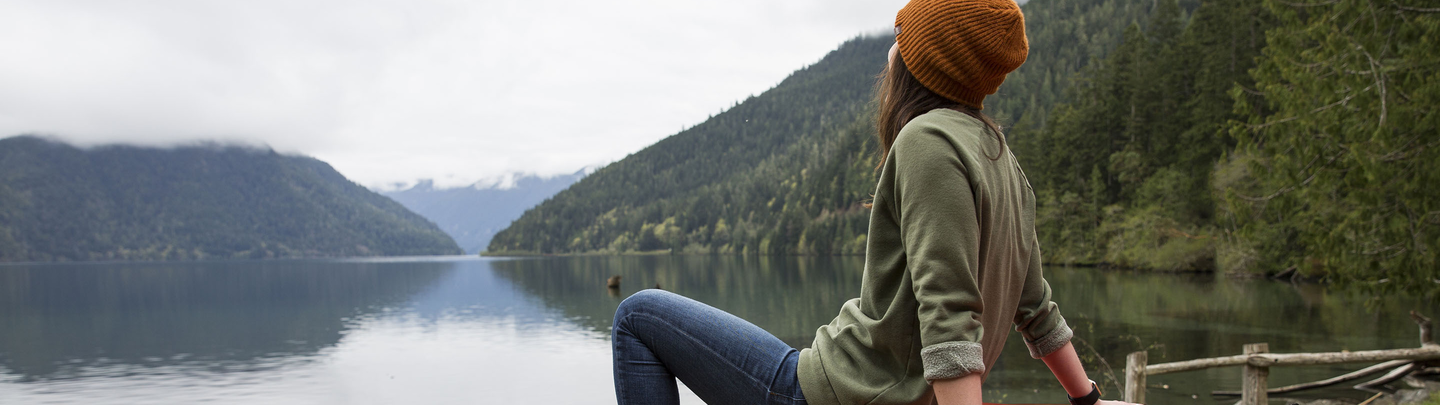 Woman sitting on the hood of a red jeep while looking at a mountain lake.