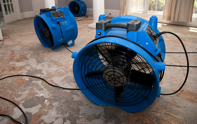 Large fans drying a room with water damage.