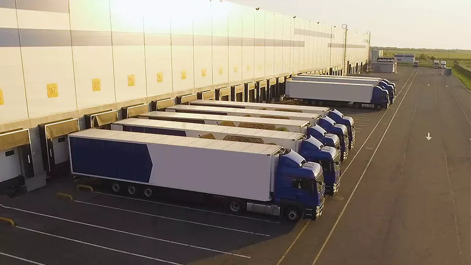 Large number of trucks in the parking lot near warehouse.