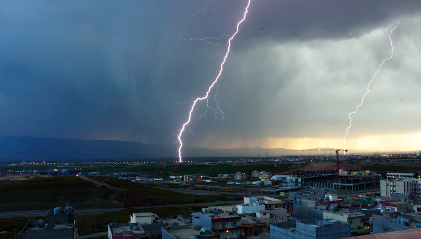 Lightnings strike in the sky over buildings.