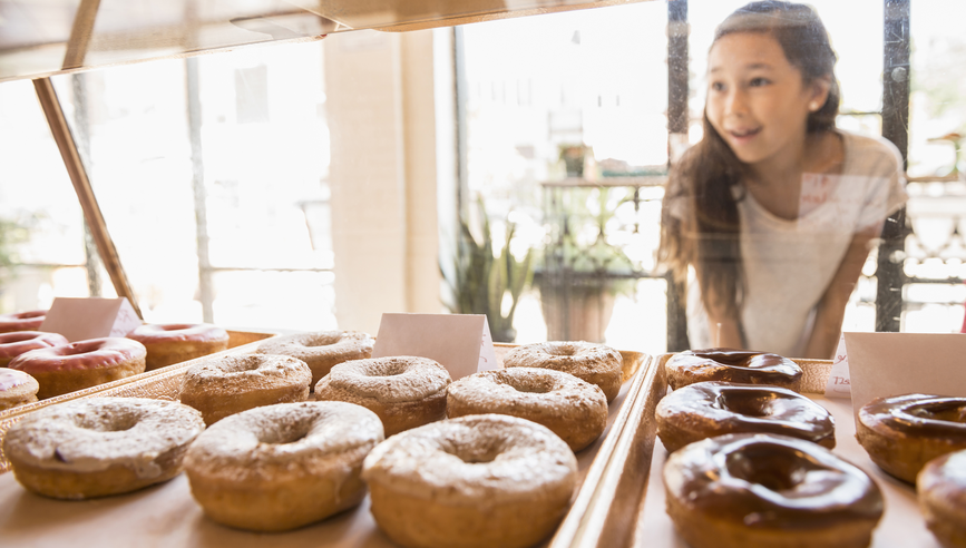 Little girl staring at donuts in a bakery display.