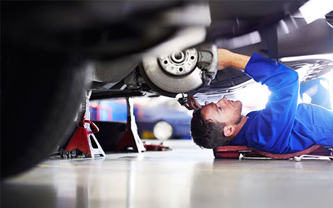Maintenance man in blue uniform fixing vehicle while on the floor