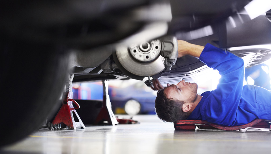 Auto mechanic in blue uniform working on a car in a shop