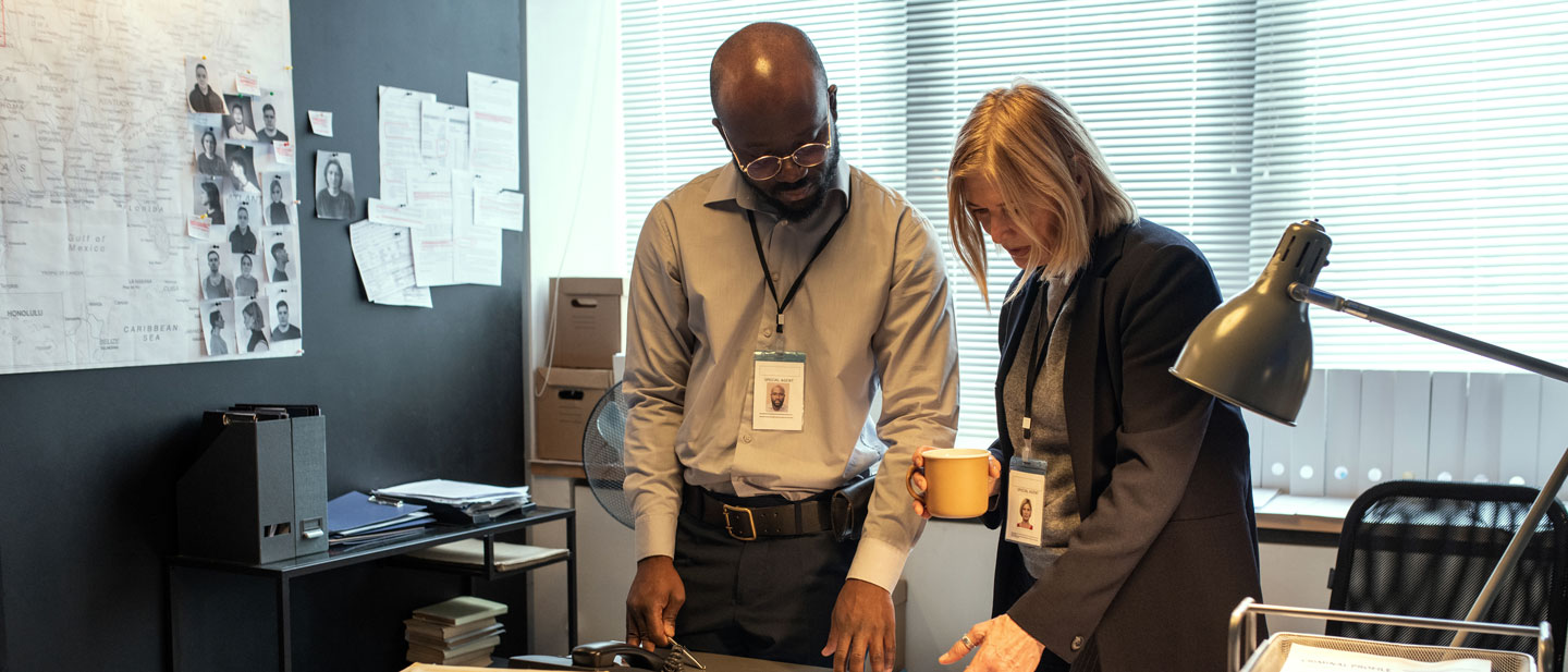 Male and female investigator standing at a desk discuss papers for a cargo theft recovery investigation.