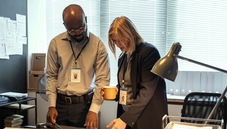 Male and female investigator standing at a desk discuss papers for a cargo theft recovery investigation.