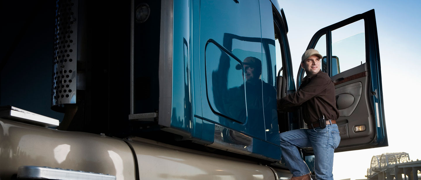 Male truck driver wearing a hat stepping into a blue semitruck with the door open, enjoying the view as he gets in.