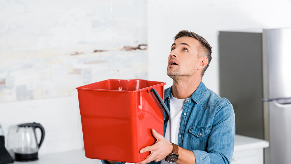 Man holding a bucket and looking up at the water leak coming from above. 