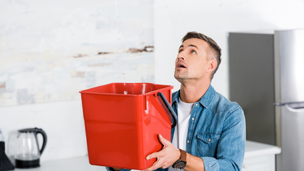 Man holding a bucket and looking up at the water leak coming from above.