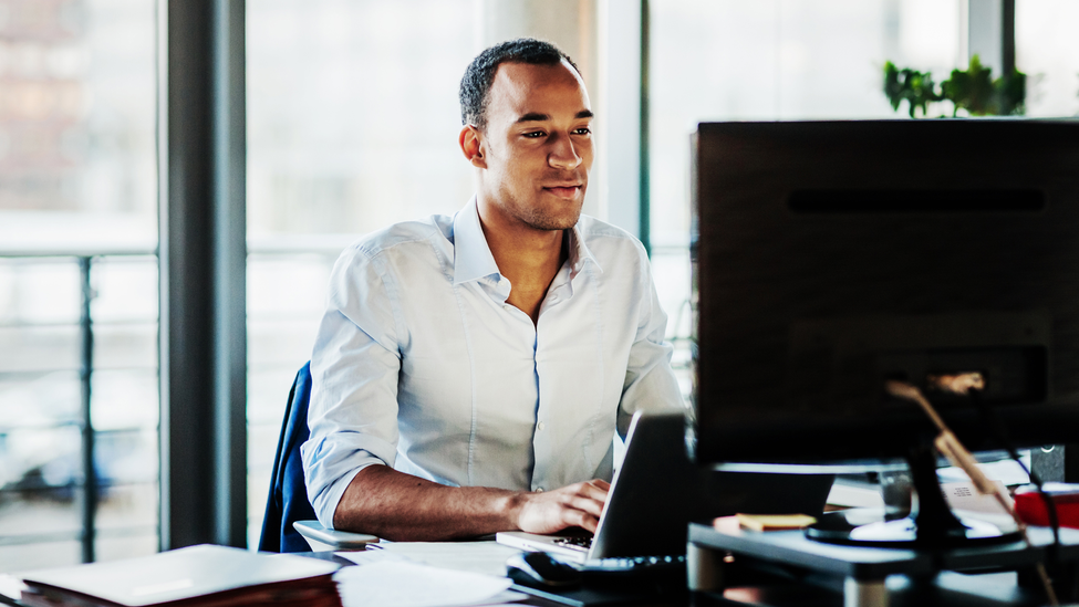 An office worker using working at his desk using a computer to review data.; Office Manager Working On Computer At His Desk