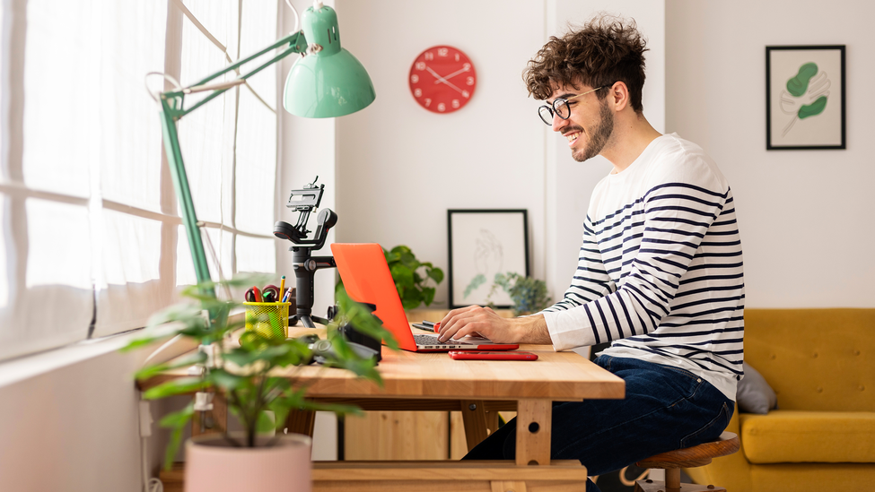 Man at computer desk with laptop and desklamp.