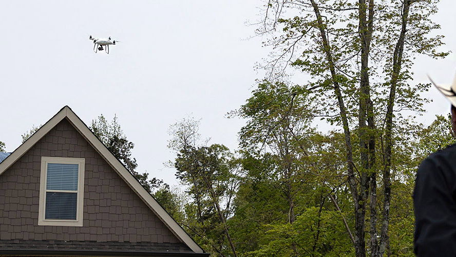 A Travelers property claim agent flying a drone over a home after a storm.