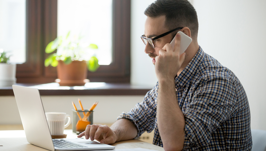 Young confident manager working on laptop and talking on smartphone.