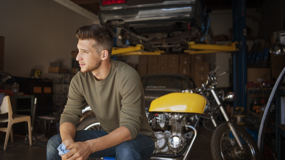 Man looking away while sitting on stool in garage.