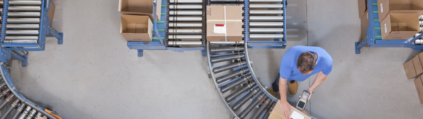 Man scanning box as it moves along assembly line.