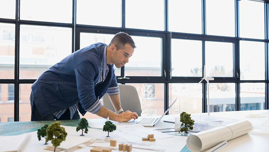 Man standing at his desk while working on laptop.