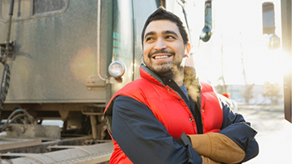 Man standing beside truck with arms folded wearing a red vest