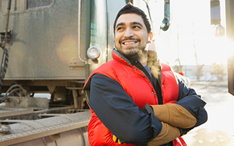 Man standing beside truck smiling with arms folded wearing a red vest
