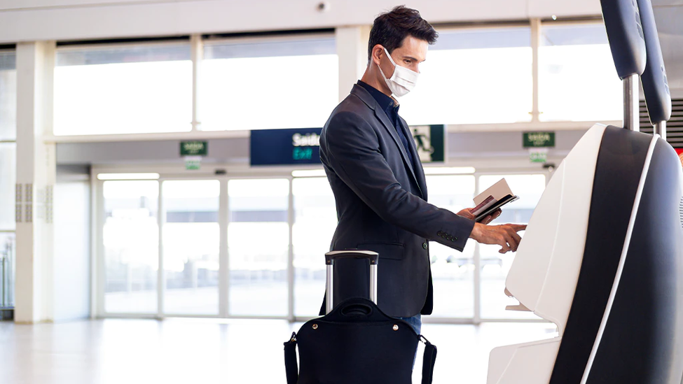 Man with medical travel insurance wearing a face mask at airport with suitcase.