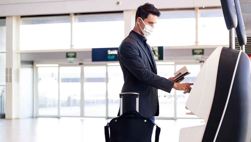 Man with medical travel insurance wearing a face mask at airport with suitcase.