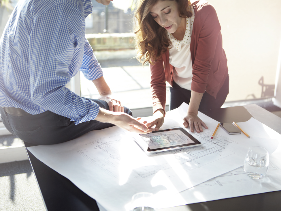 Two businesspeople discuss architectural plans in an office.