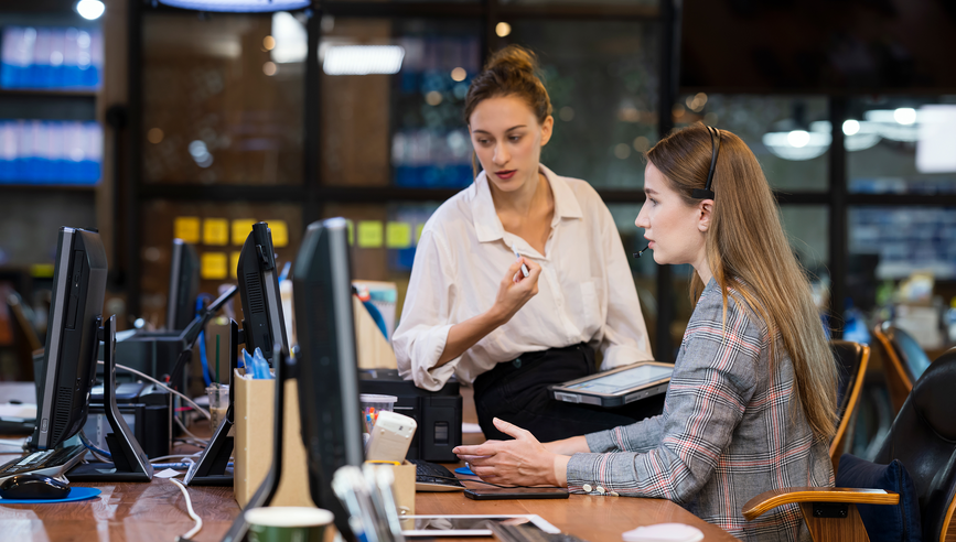 Manager and employee looking at computer while discussing training at desk.
