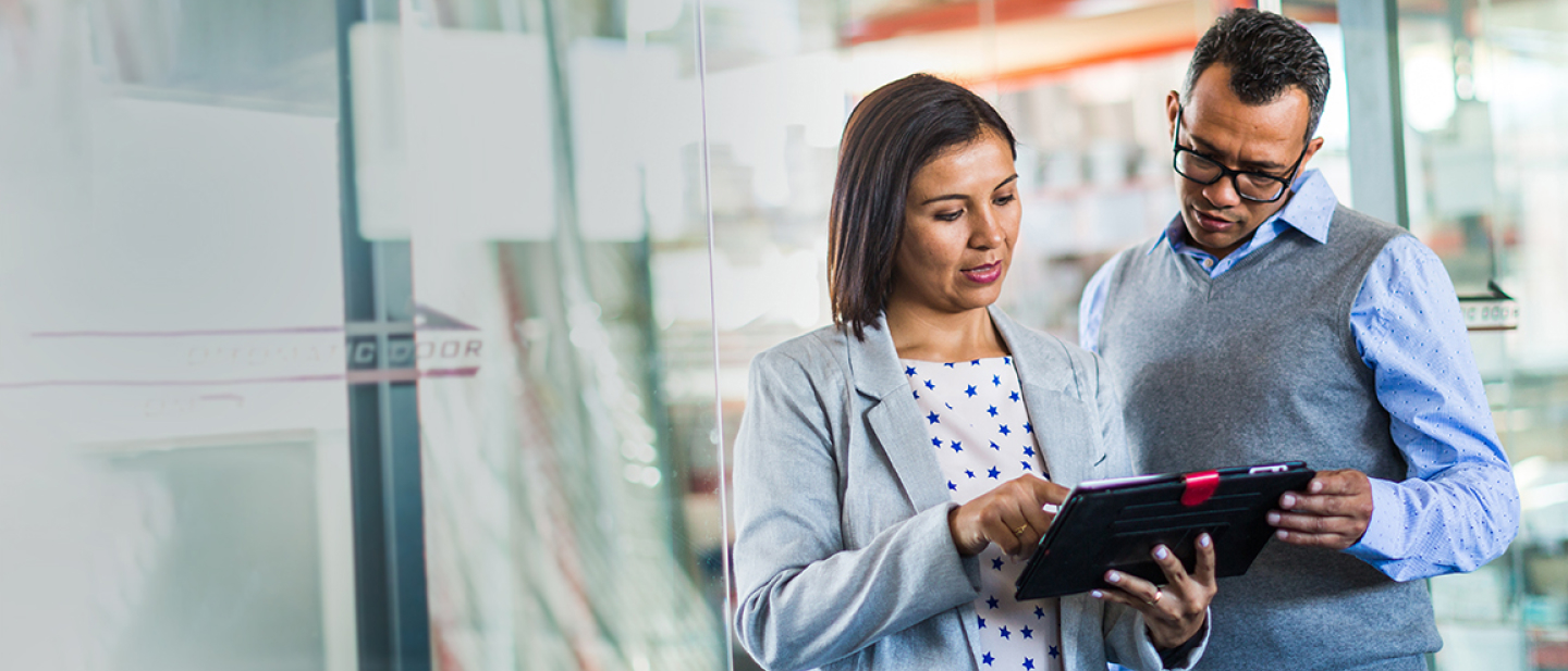 Small business owners discuss insurance coverage while standing in a glass-walled store office.