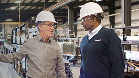 Two men in hard hats discussing manufacturing insurance in a plant.