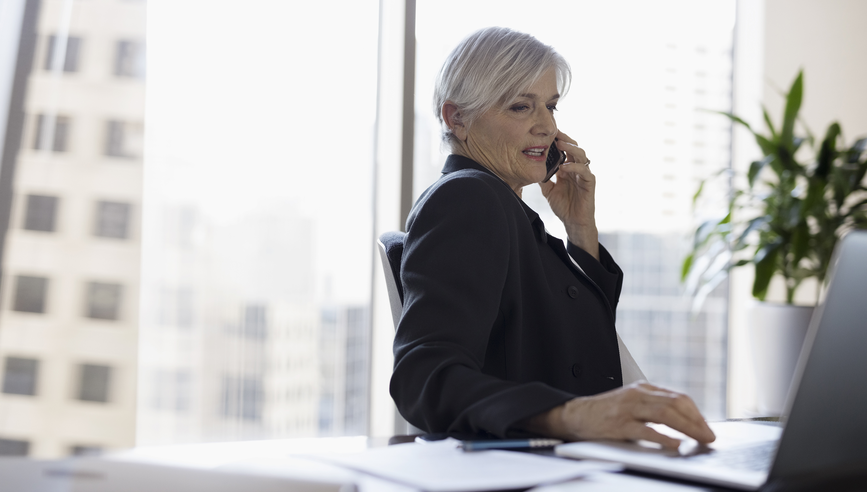 Senior female lawyer working at laptop and talking on cell phone